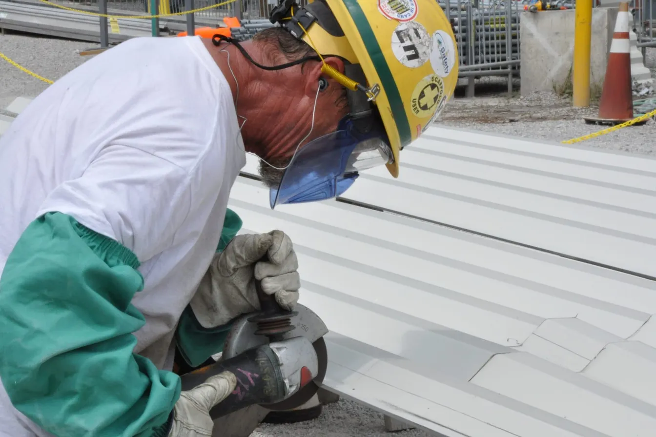 Trabajador con careta, casco y guantes usando una esmeriladora angular con guarda y mango lateral