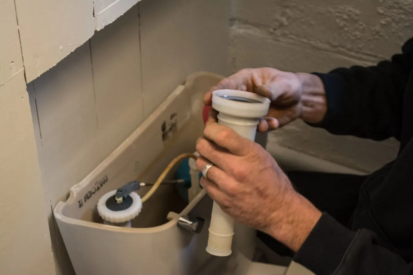 Manos cambiando la válvula dentro del tanque de un WC