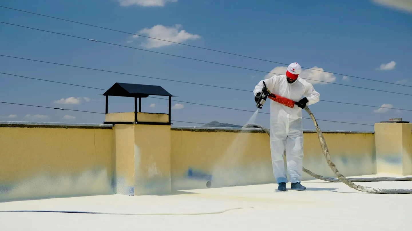 Persona aplicando impermeabilizante blanco sobre una azotea