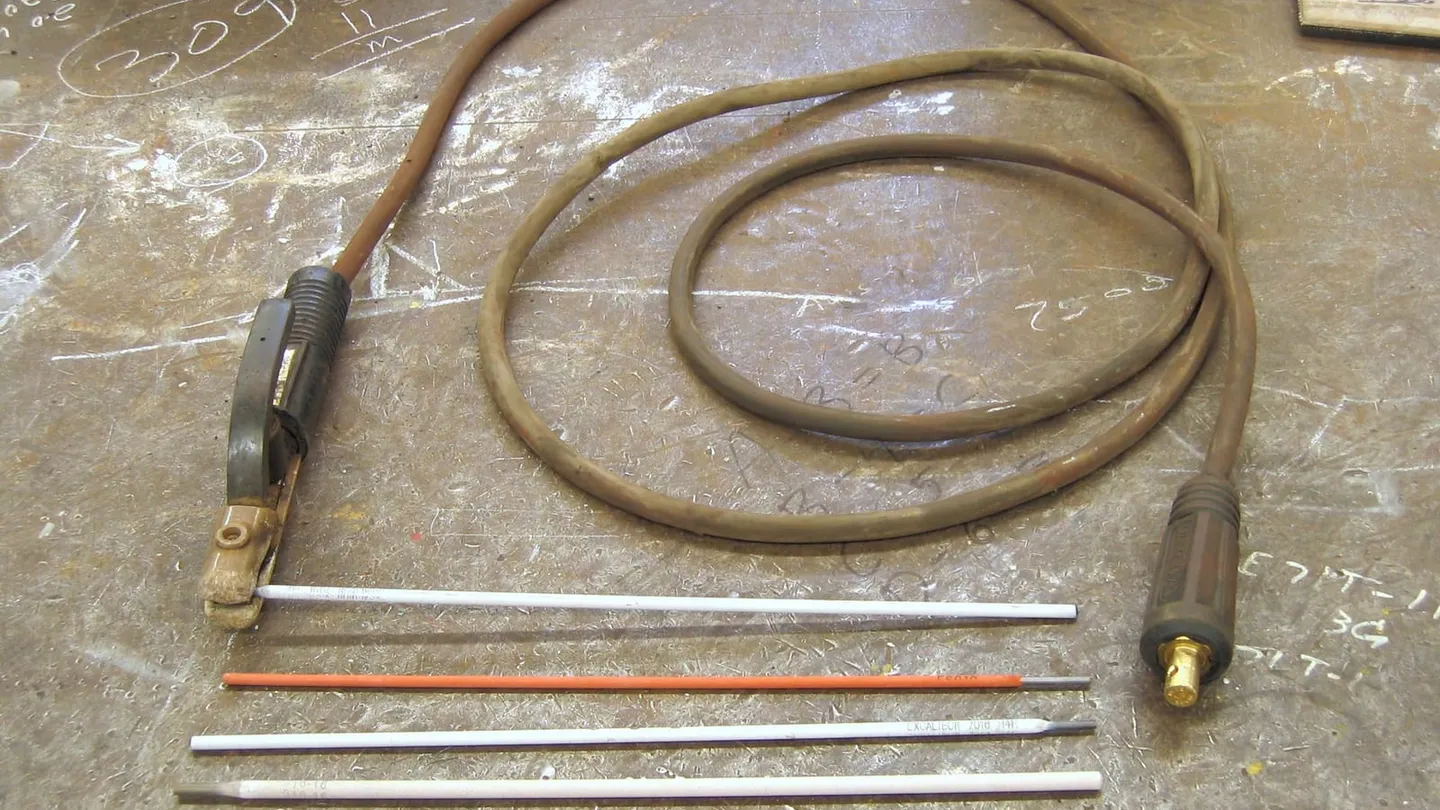 Portaelectrodo con su cable y cinco electrodos de distinto recubrimiento sobre una mesa de soldar